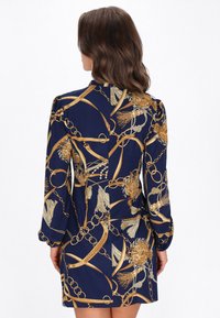 Hosszú ujjú tengerészkék ruha aranylánccal és virágmintával, sima anyagból, testhez simuló sziluettel, és vállnál gyűrt részletekkel.