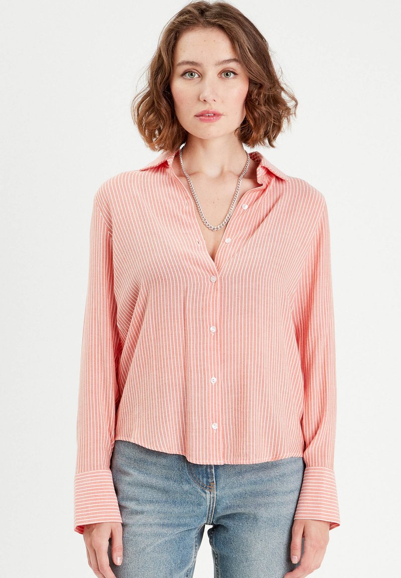 Chemise à boutons rayée rose avec des manches longues et amples et un col. Tissu léger avec une coupe décontractée ; comporte des boutons blancs sur le devant.