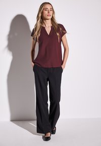 Blusa corto maniche in bordeaux con scollo a V, abbinata a pantaloni neri a gamba larga e scarpe nere. Tessuto morbido, vestibilità comoda, decorazioni minime.
