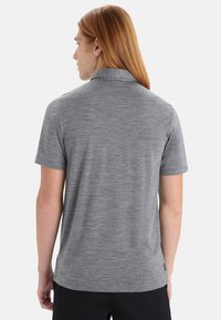Šedá polo košile s krátkým rukávem, vyrobená z hladké tkaniny, s límečkem a jemnou texturou. Pohled zezadu ukazuje detaily na ramenou.