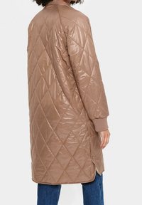 Manteau long matelassé dans une teinte marron chaud, avec des motifs en losange, des poignets côtelés et des fermetures à boutons sur le côté. Fini texturé et brillant.