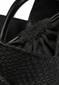 Melnas austas ādas somas ar savelkamu auduma iekšpusi, kvadrātveida formu un strukturētu rokturi drošai nēsāšanai.