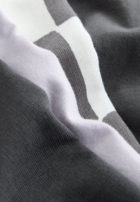 Nærbillede af blødt, strikket stof med hvide, grå og sorte horisontale striber, der viser tekstur og blide folder.