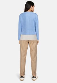 Veste ajustée en daim bleu clair avec manches longues, design sobre et détails de couture au dos. Associée à un pantalon beige et des baskets décontractées.