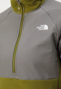 Giacca in fleece grigia e verde con mezzo zip, dotata di colletto alto e logo The North Face in bianco sul lato sinistro del petto.