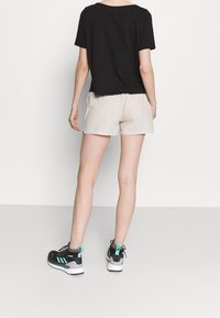 Top negro de manga corta, pantalones cortos beiges y zapatillas negras con acentos en azul turquesa. El material parece casual; el diseño es simple y relajado.