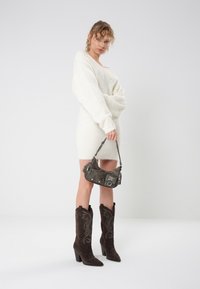 Vit fluffig klänning i tröjastil, bruna mocka cowboy stövlar med broderade detaljer, och en grå handväska med silveraccenter och rem.