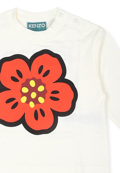 Chemise blanche à manches longues avec un grand motif de fleur rouge avec des contours noirs, des centres jaunes et des détails de boutons au niveau du col.