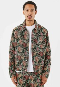 Blomstret denimjakke med en mørkegrøn baggrund og rosa, røde og gule roser, metalknaplukninger og en brystdetalje.