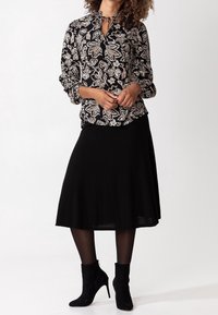Camicia nera a maniche lunghe con un motivo floreale in crema, caratterizzata da un nodo al collo. Abbinate a una gonna nera a ruota e stivaletti.