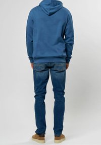 Sudadera con capucha azul, corte holgado, fabricada con una mezcla de materiales. Combinada con jeans de un azul claro, de corte recto, con un ligero desgaste, y zapatillas de ante en color tostado.