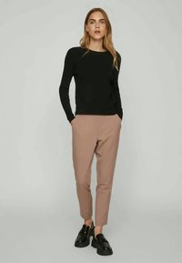 Suéter negro ajustado, pantalones beige a medida y mocasines negros. Textura suave con detalles de diseño mínimos. Atuendo simple y moderno.