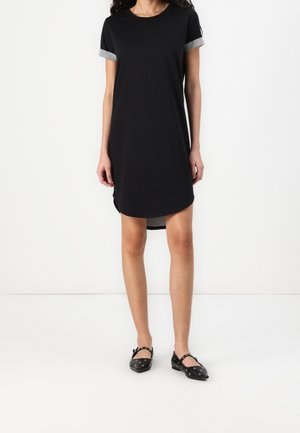 Abito nero con maniche corte arrotolate grigie, vestibilità rilassata, orlo arrotondato e spacchi laterali. Indossato con ballerine nere con ritagli rotondi.