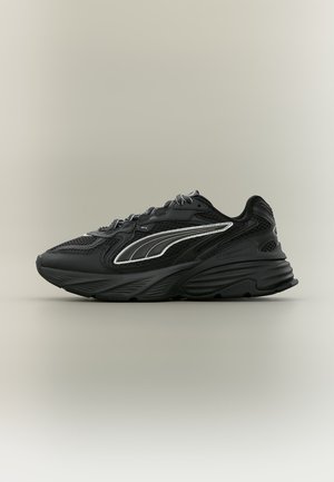 Baskets de sport noires avec des panneaux en mesh, une semelle épaisse et rembourrée, et un motif argenté réfléchissant en forme de swoosh sur le côté, vues de profil.