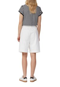 Białe bawełniane szorty o luźnym kroju, zestawione z czarno-białą paskowaną crop topem. Stylizacja obejmuje białe trampki z czarnymi akcentami.