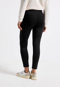 Leggings neri con una superficie liscia, design aderente e vita alta. Abbinati a scarpe da ginnastica bianche con un accento metallico.