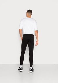 Svarta joggers med en smal passform och ribbade ankelslut, tillsammans med en enkel vit t-shirt. Byxorna har en bakficka.