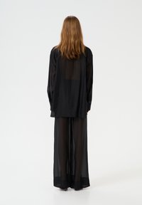 Black translucent ensemble featuring a loose-fitting shirt and wide-leg pants, both made of lightweight fabric.
