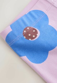 Zložena rožnata tkanina z velikim modrim cvetličnim tiskom in rjavim krožcem z belimi pikami na detajlu sredinskega šiva.