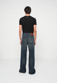 Tricou negru și blugi largi de culoare albastru închis cu buzunare pe spate și o etichetă din piele a brandului. Textură netedă, design casual.