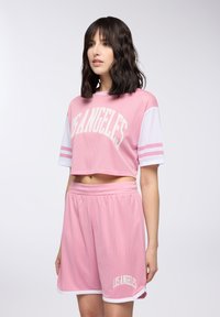 Różowy siatkowy crop top z napisem "LOS ANGELES", w połączeniu z pasującymi różowymi szortami z białymi akcentami i luźnym fasonem.