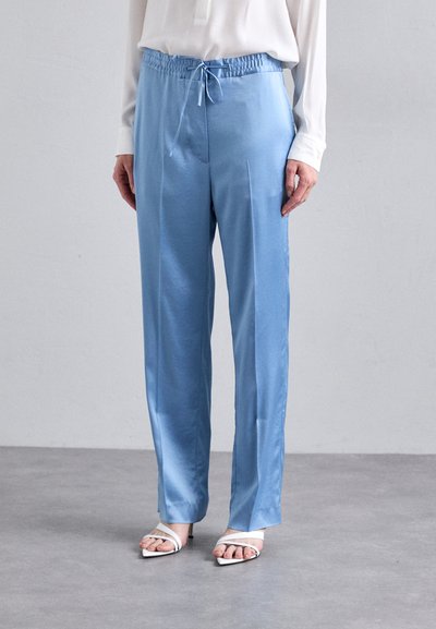 Light blue satin pants with an elastic waistband and drawstring detail. Smooth texture with a loose fit, paired with white heeled sandals.