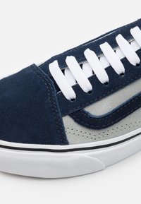 Baskets en daim bleu avec des accents gris, des lacets blancs et une semelle noir et blanc présentant une finition texturée et des détails cousus.