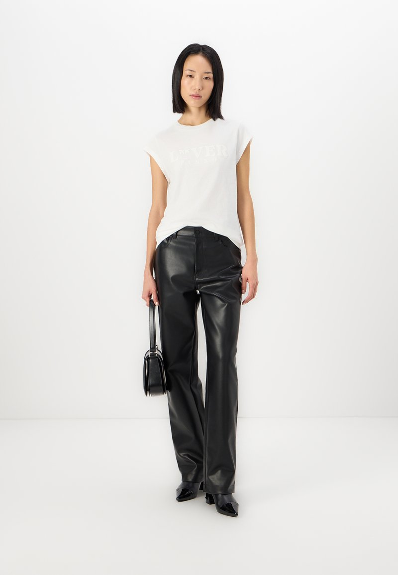 Witte T-shirt met korte mouwen en reliëftekst, gecombineerd met zwarte leren wijde broek en een kleine zwarte handtas; glanzende textuur.