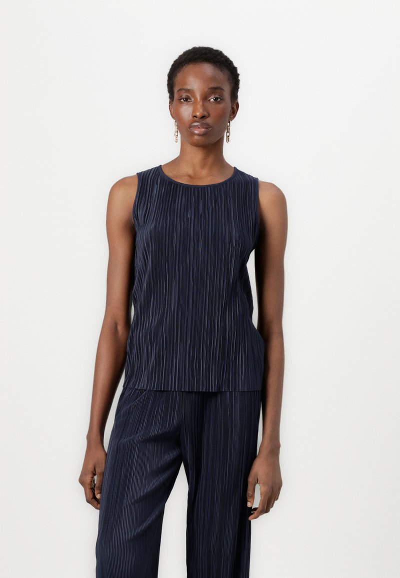 Navy pleated sleeveless top, featuring a round neckline and textured fabric, with a soft drape extending to the waist. Coordinating pants visible.