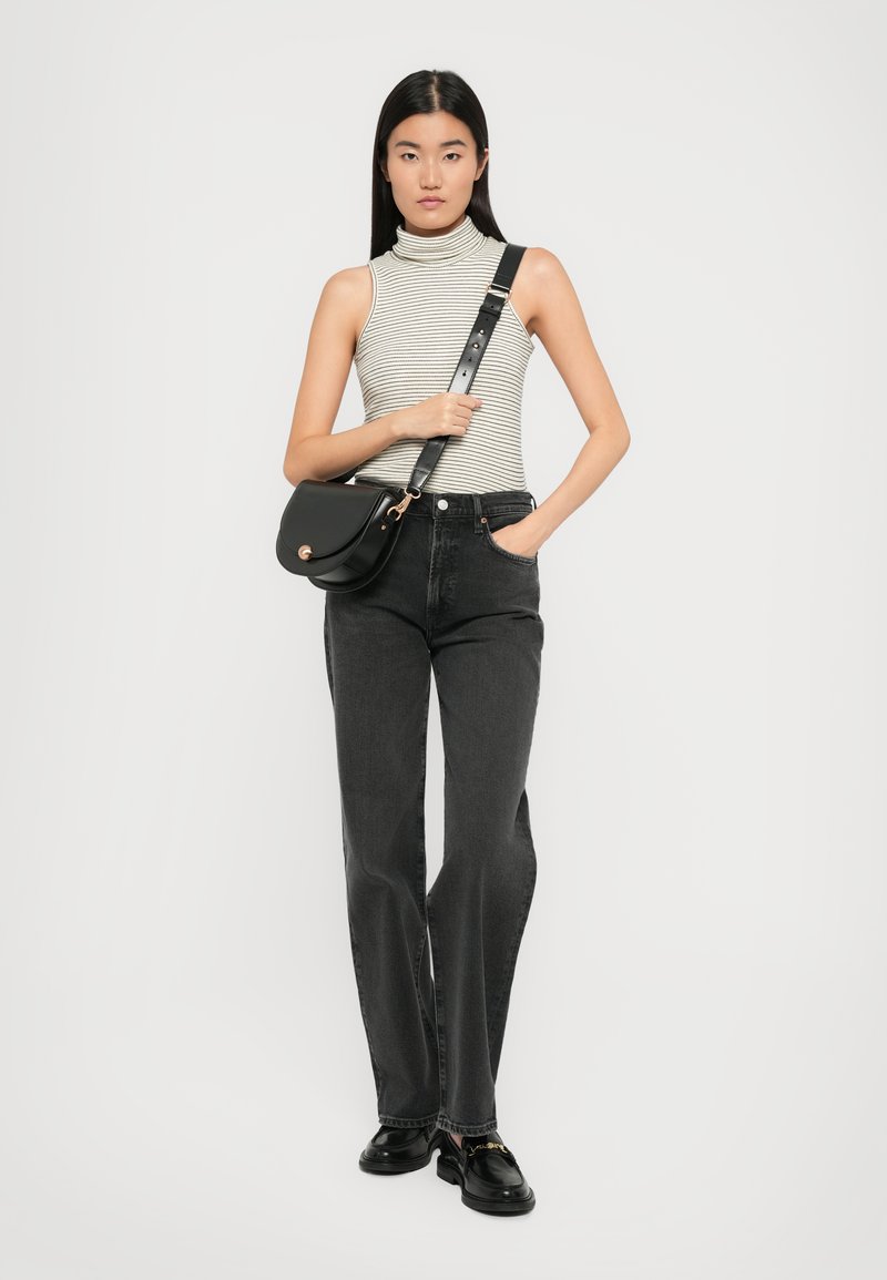 Jean noirs taille haute, un pull à col roulé rayé ajusté, et un sac bandoulière noir avec un fermoir circulaire. Des mocassins noirs complètent la tenue.