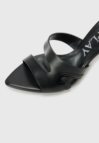 Sandale à talons en cuir noir avec un embout carré, présentant deux brides croisées et de délicates coutures sur le côté. Texture lisse.