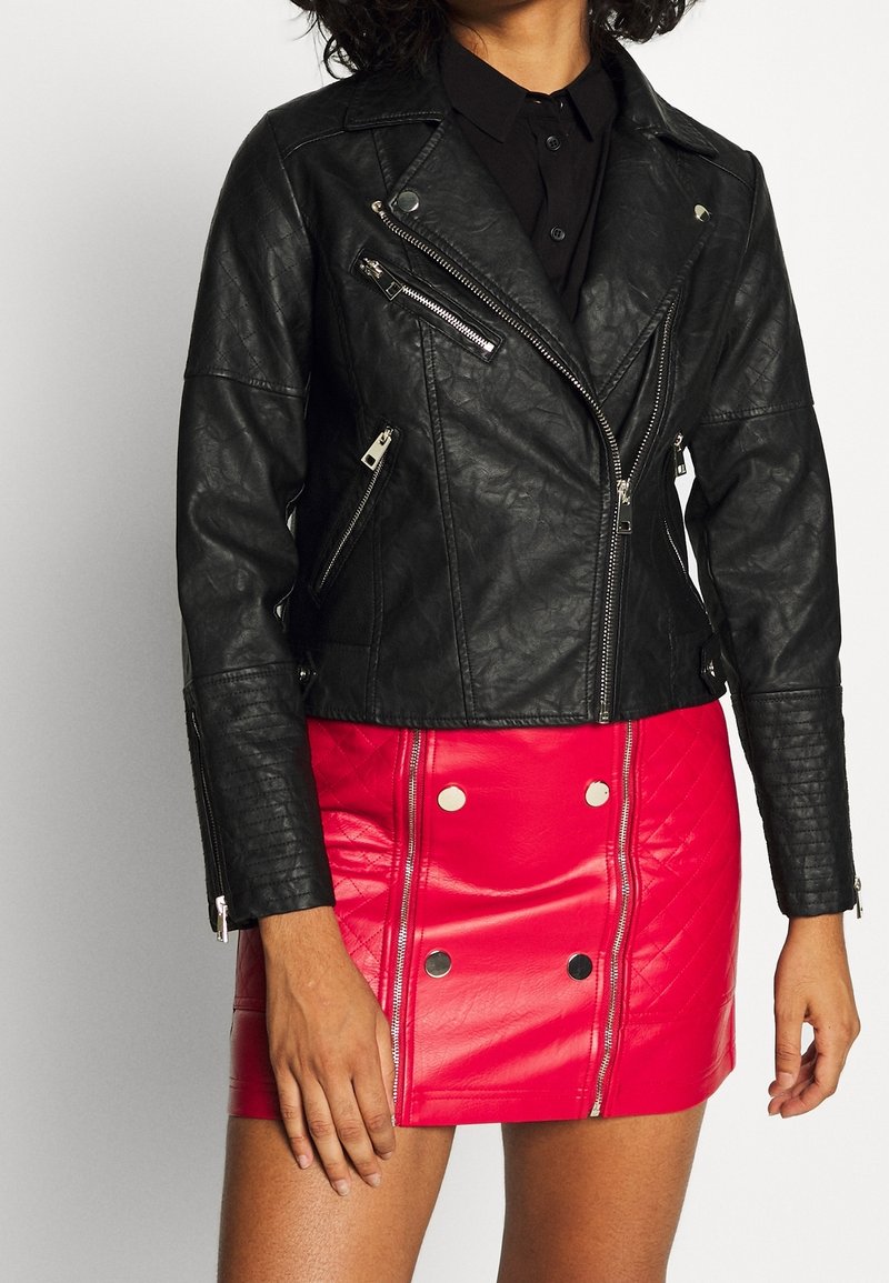 Donna che indossa una giacca di pelle nera con zip sopra una mini gonna di pelle rossa con dettagli di bottoni e zip.