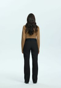 Zwarte skibroek gecombineerd met een lange mouwen bruin top, met een rechte pasvorm en ritsen bij de enkels. Gladde stoftextuur, minimalistisch ontwerp.