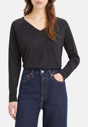Black long-sleeve V-neck sweater made of soft fabric, paired with high-waisted dark blue jeans, featuring prominent stitching and pockets.