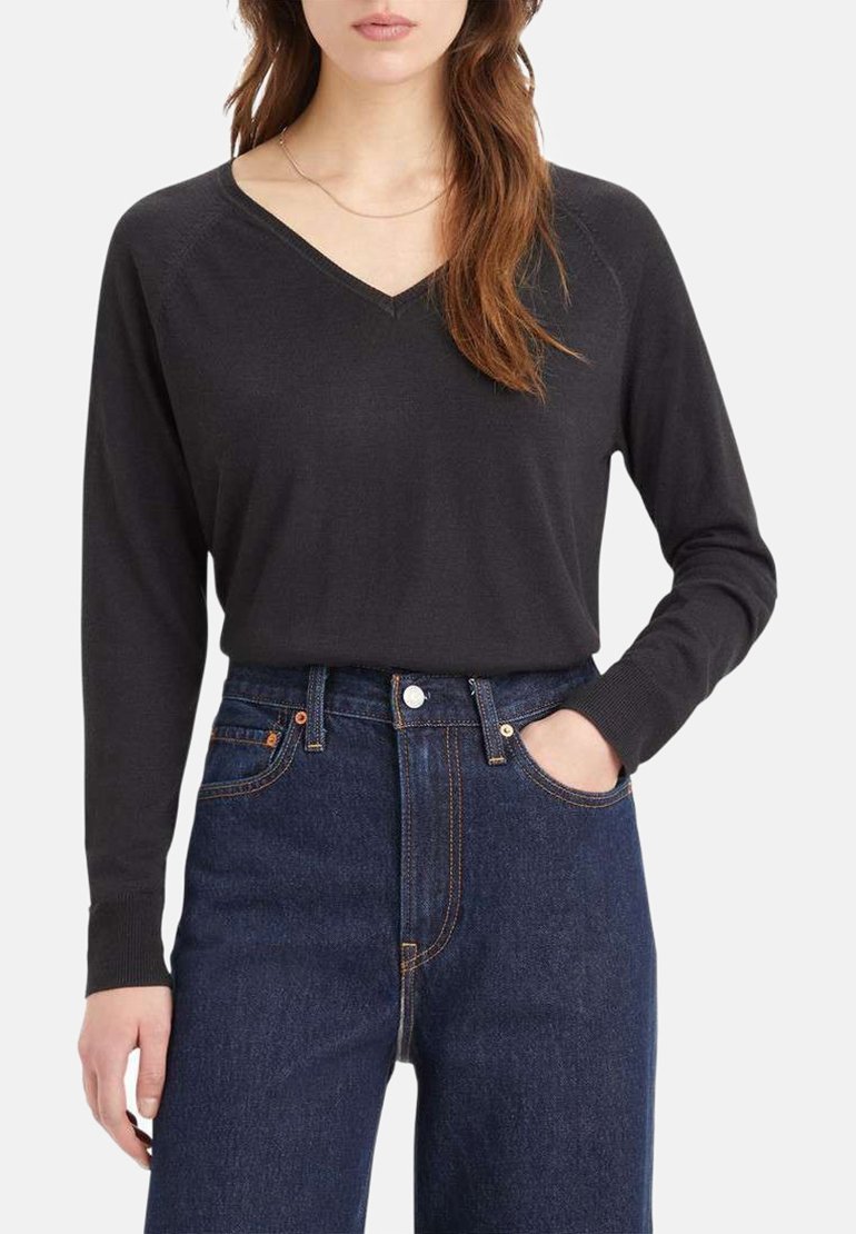 Maglione nero a maniche lunghe con scollo a V, realizzato in un tessuto morbido, abbinato a jeans blu scuro a vita alta, caratterizzati da cuciture evidenti e tasche.