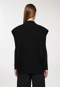 Gilet di lana nera a vestibilità ampia, con spalle larghe e un motivo texture. Il colletto è a coste, adatto per essere indossato sopra altri capi.