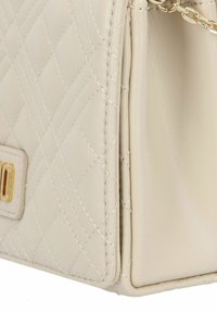 Beige quilted leather handbag with gold hardware, featuring a chain strap, stitched detailing, and a rectangular shape.