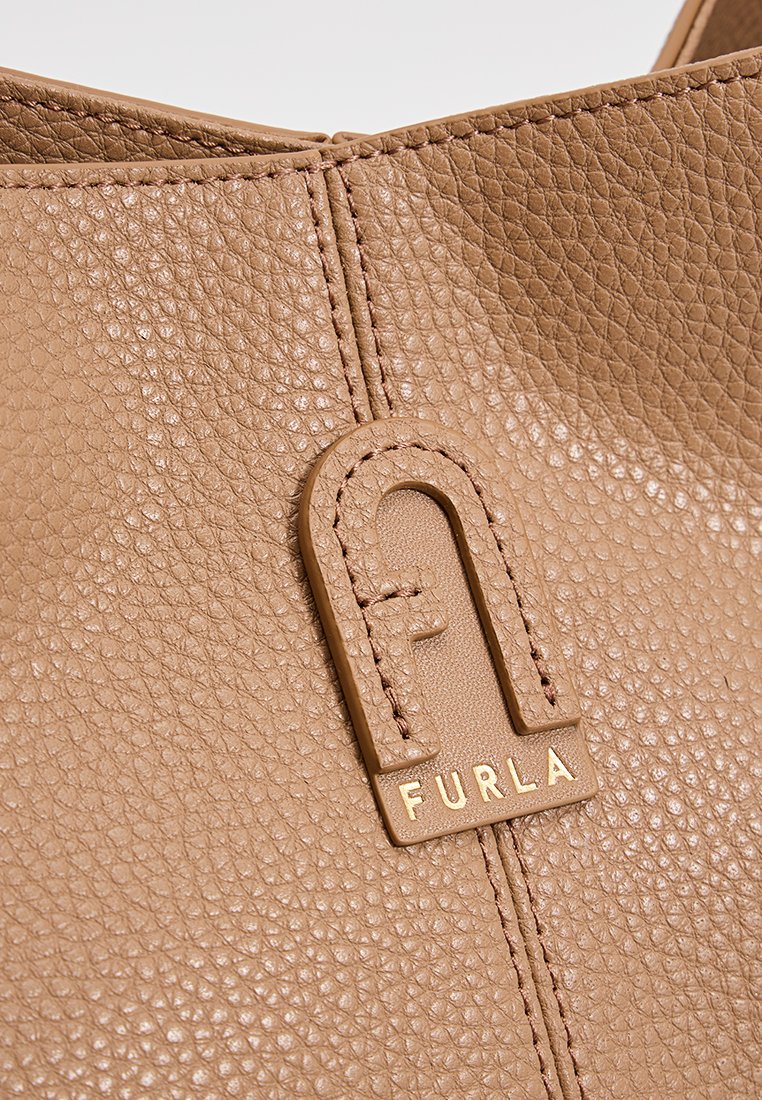 Beige Lederhandtasche mit texturierter Oberfläche, ausgestattet mit einem goldfarbenen "Furla"-Logo-Akzent und genähten Details.
