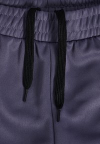 Lilla atletikshorts med elastisk talje, der har sorte snore og en tekstureret stofoverflade.