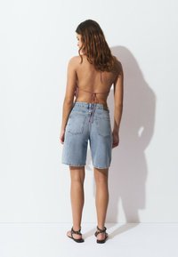Pantalones cortos de mezclilla en azul claro con una cintura alta, con bolsillos traseros y un dobladillo deshilachado. Combinados con una blusa morada con tirantes y sandalias.