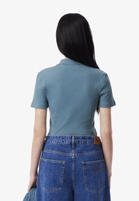Ljusblå rummig pikétröja med korta ärmar, kombinerad med hög midja-jeansshorts som har en läderlapp och två bakfickor.