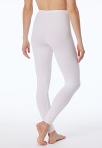 Leggings en coton blancs avec une coupe ajustée, texture unie et taille haute, montrés de dos avec des pieds nus visibles.