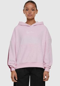 Roze hoodie met een voorzak, witte tekstlogo en contrasterende mouwaccenten. Zacht materiaal en een relaxte fit.