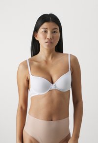 White padded bra with adjustable straps and a small bow detail at the center. Background is plain, highlighting the product's design and color.