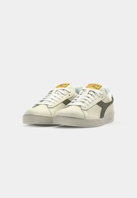 Sneakers in off-white leather with green accents, textured suede, and light blue lining. Features white laces and a yellow tongue label.