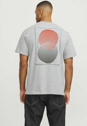 Grijze t-shirt met korte mouwen, met een grafisch ontwerp van een rood- en zwartgestreept cirkelpatroon op de achterkant. Standaard pasvorm en zachte textuur.