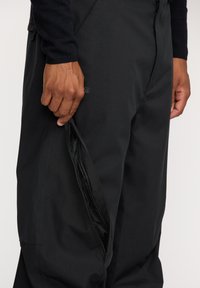 Pantalons étanches noirs avec une finition texturée, dotés d'une poche latérale avec fermeture éclair et d'une coupe ajustée à la taille.