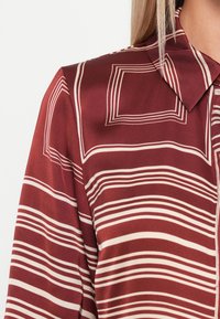 Bordått blus med vita horisontella ränder och fyrkantiga mönster, med krage och slät satintextur.