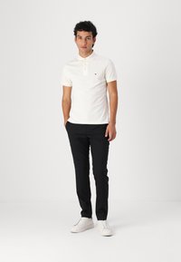 Polo à manches courtes blanc avec patte de boutonnage à trois boutons, pantalon noir et baskets blanches. Présente un petit logo coloré sur la poitrine.