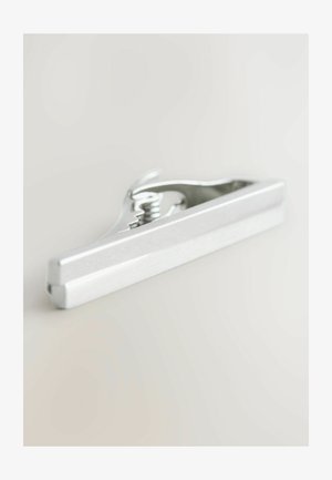 Silberner Metallclip mit einem Federmechanismus, der eine glatte, verlängerte Form und eine strukturierte Grifffläche aufweist. Einfaches Design, funktionale Hardware.